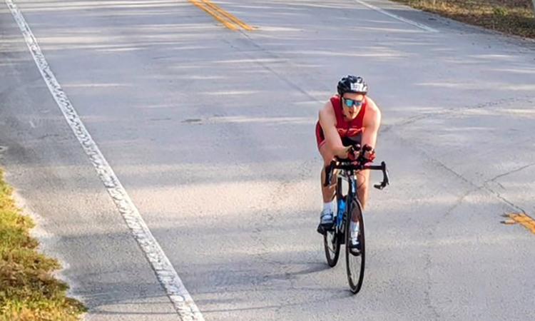 Jacob Beldick riding his bike on a two-lane road during the cycling portion of the Ultraman Florida triathlon.